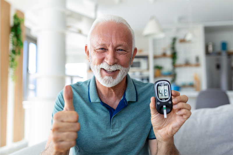 A man holding his blood glucose monitor up to the camera and smiling with a thumb up. 
